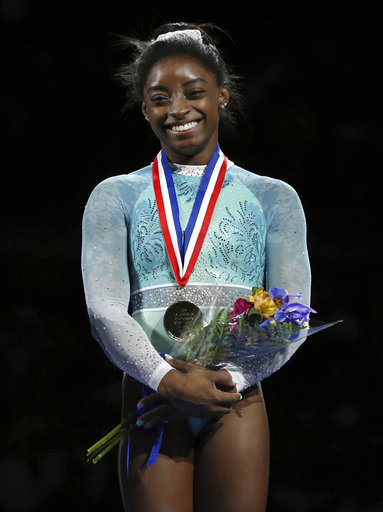 Simone Biles in her teal leotard, supporting the victims of Larry Nassar, with her gold medal and commemorative flowers.