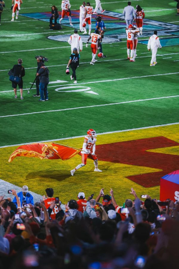 Chiefs player number 21, Trent McDuffie, running down the field with a Chiefs flag after their win.