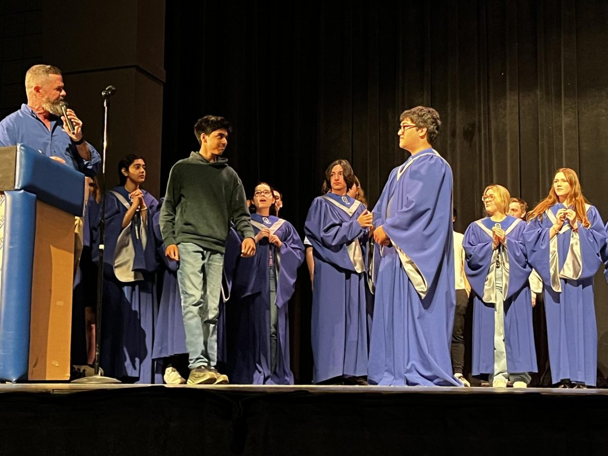 Arya Prakash '28 walks across the stage to receive his robe and be inducted into varsity chorale. Drew Schlageter '25 helped him get the robe on to induct him. “I almost tripped over my robe, but it was still fun” Prakash said.